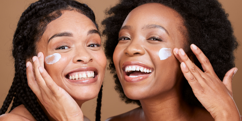 Two smiling women moisturizing their faces with lotion