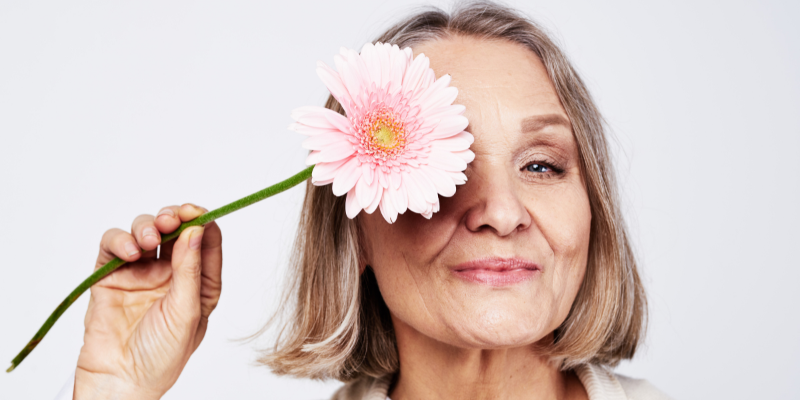 Older woman smiling and holding a pink flower in front of her face