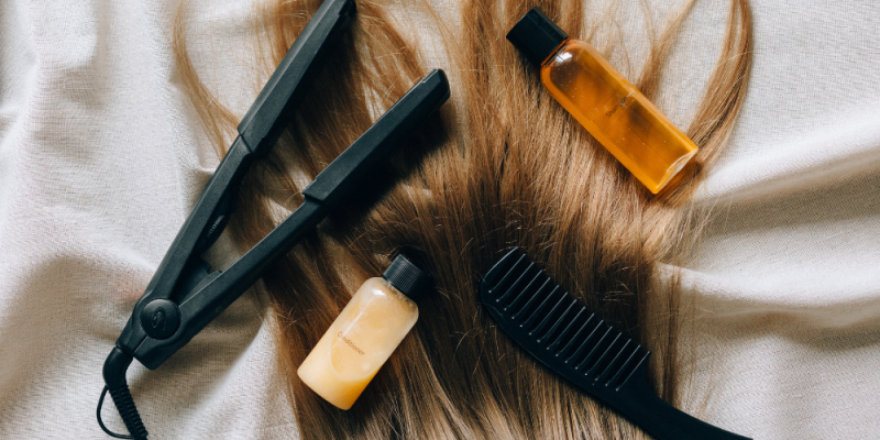 Hair styling tools and products stylistically arranged atop locks of brown hair